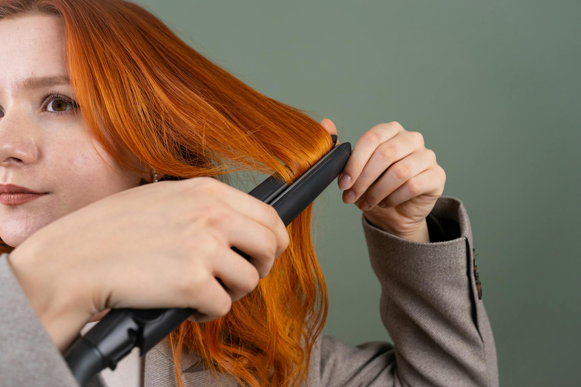 woman styling hair with hair straightener close up